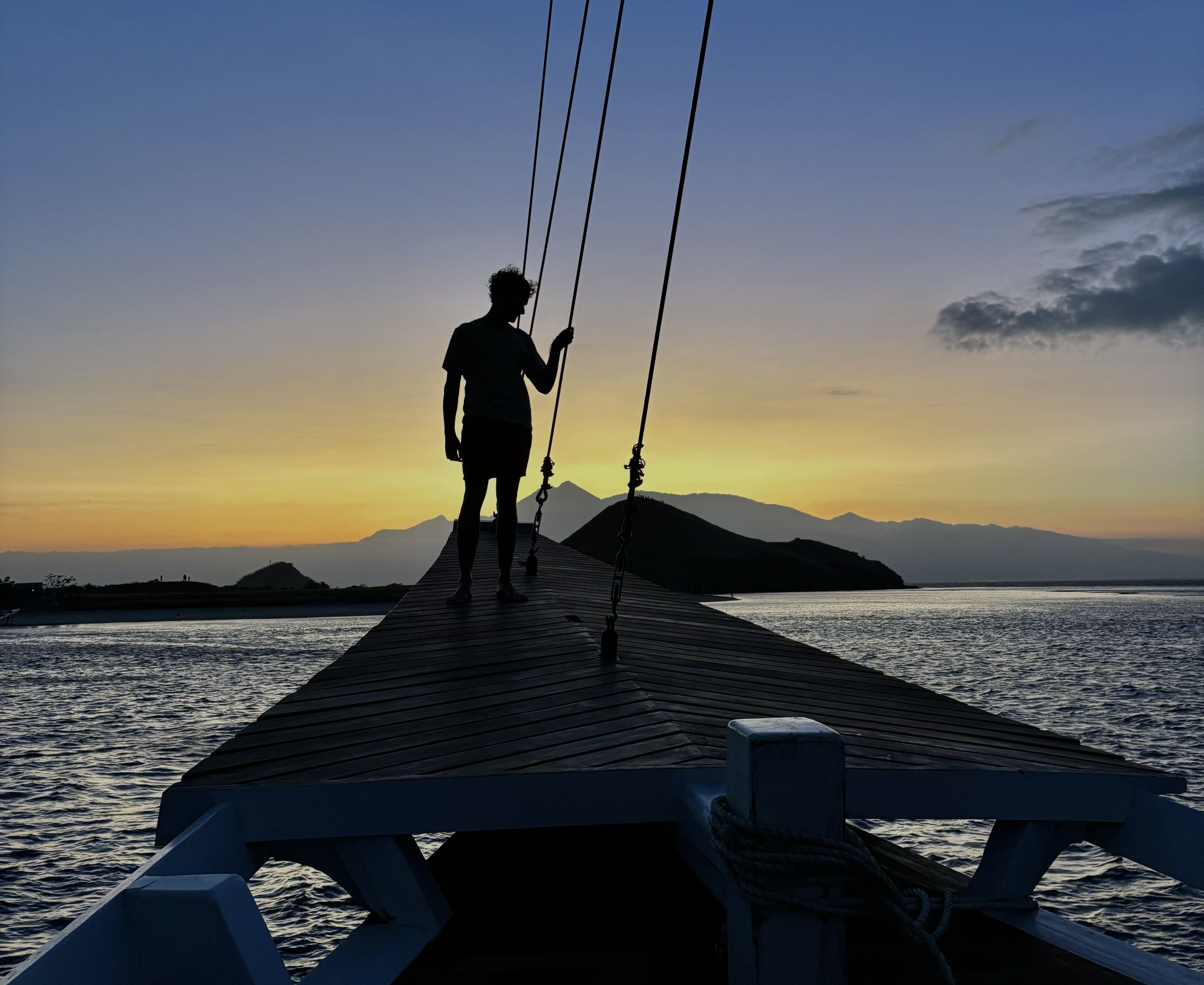 Viaggiatore sul ponte della barca Putri Naga al tramonto, durante una crociera nel Parco Nazionale di Komodo.