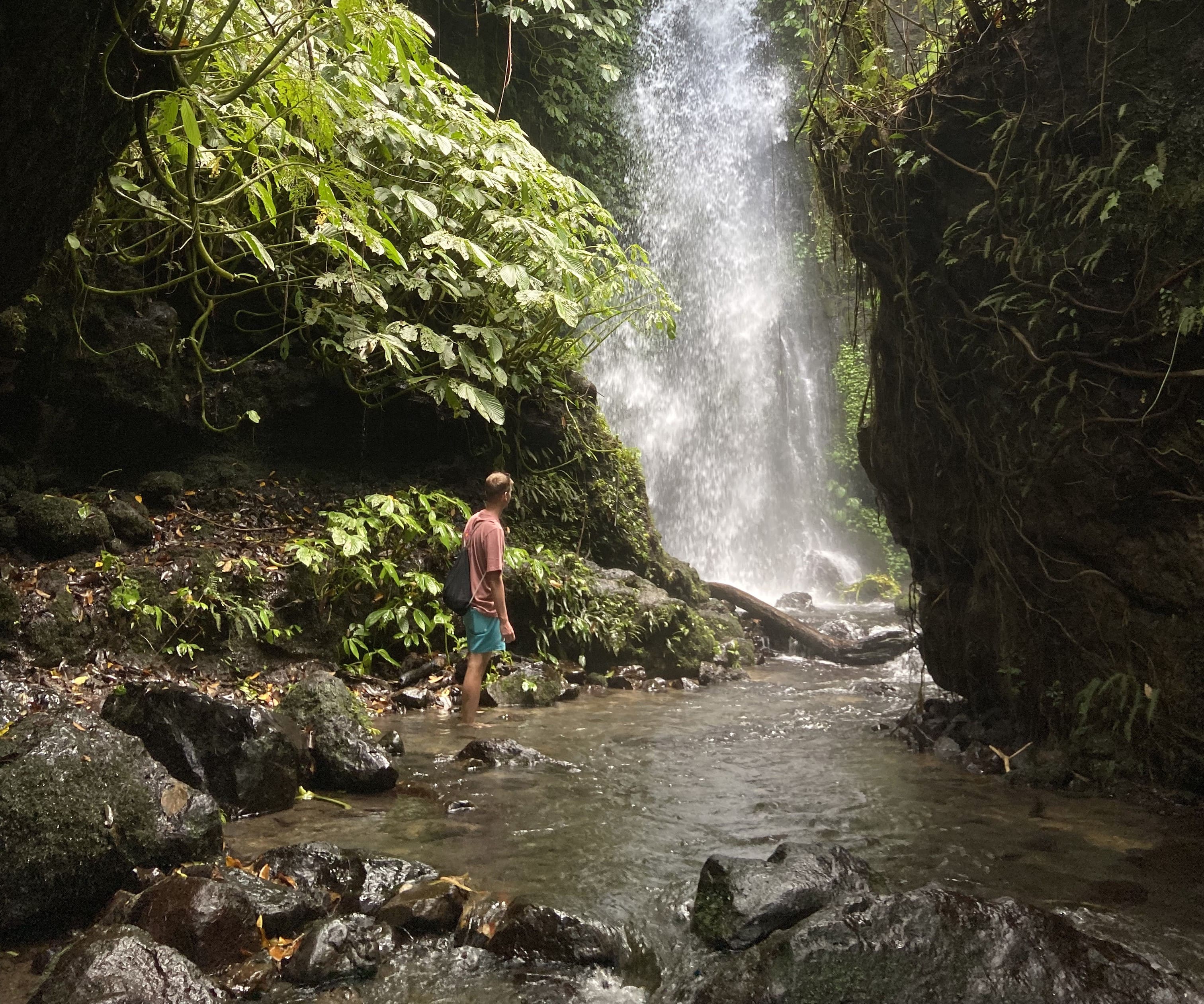 Viaggiatore che esplora una cascata nascosta nella giungla tropicale durante un trekking a Bali.