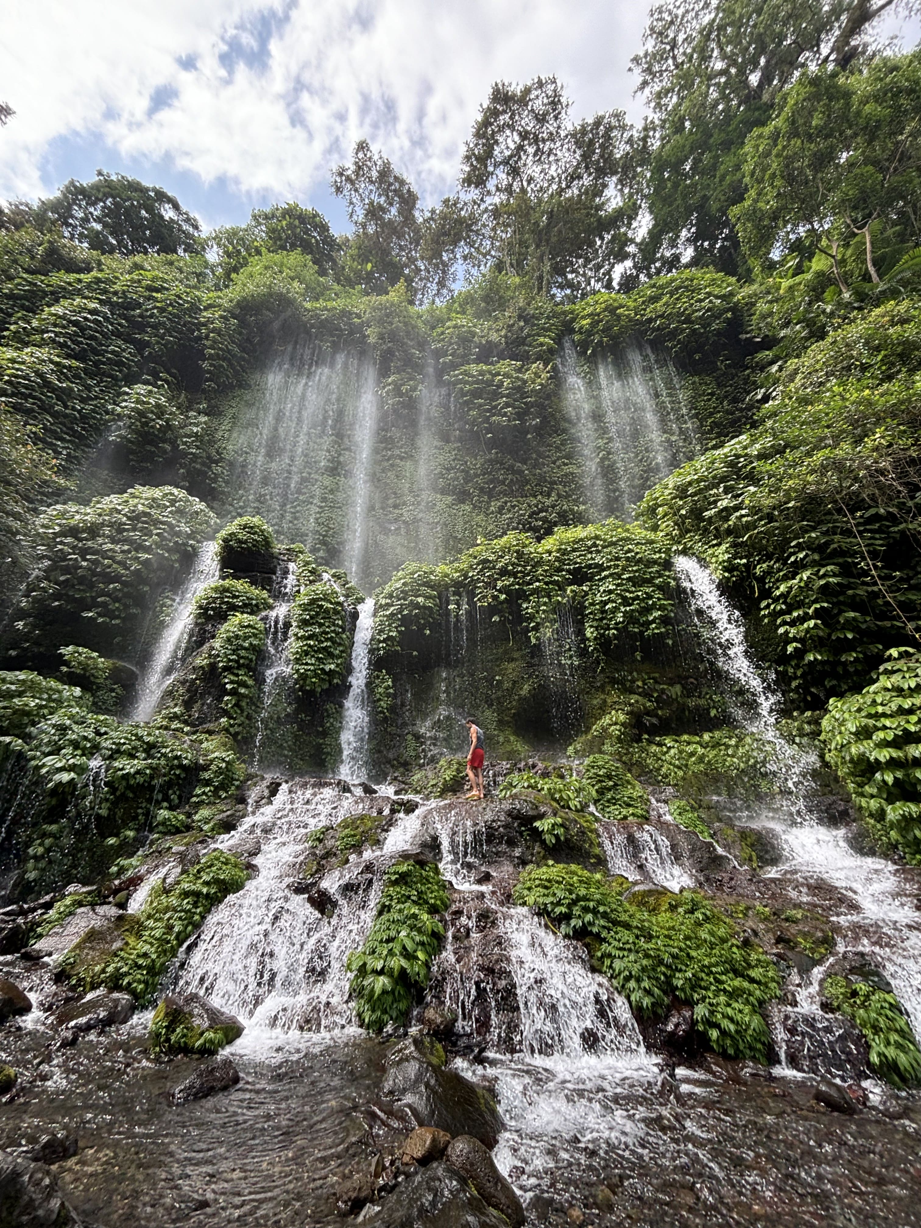 Viaggiatore ai piedi di una cascata tropicale circondata dalla giungla, durante un tour avventura a Bali.