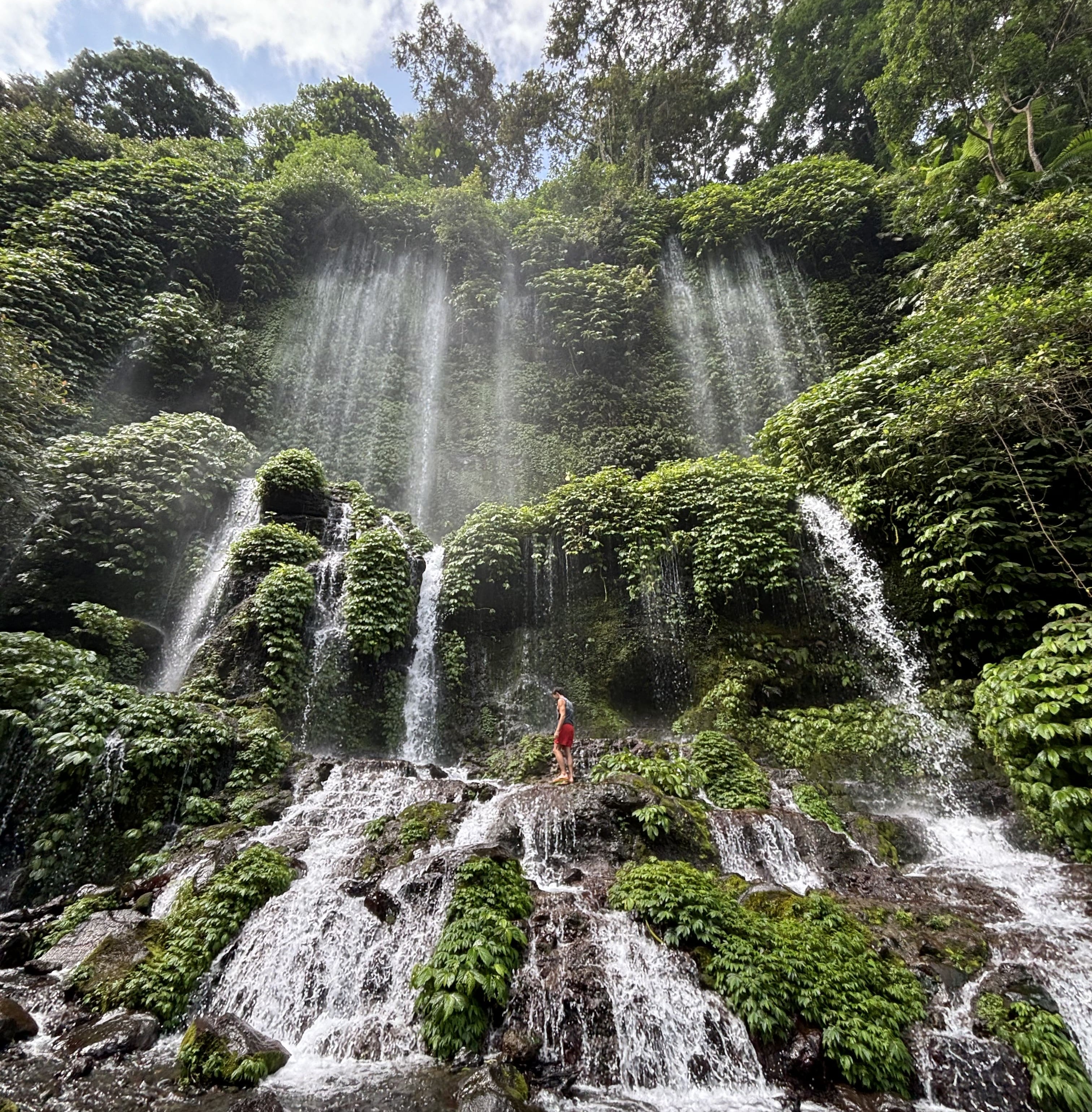 Viaggiatore ai piedi di una cascata tropicale circondata dalla giungla, durante un tour avventura a Bali.