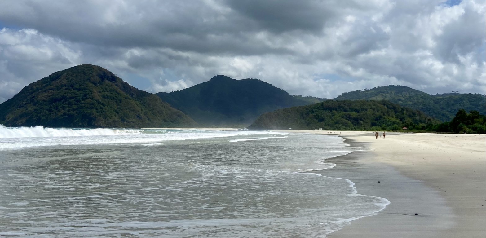 Spiaggia tropicale di Lombok con mare turchese e montagne sullo sfondo, ideale per relax e surf in Indonesia.